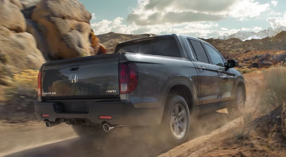 A grey 2022 Honda Ridgeline is shown from the rear driving on a dusty dirt road.