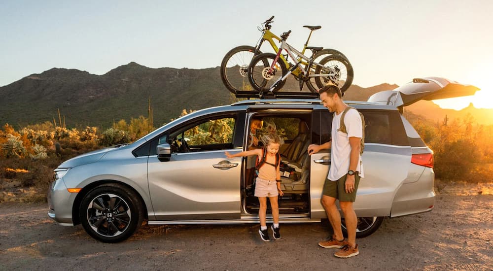 A family is shown getting out of a silver 2022 Honda Odyssey near a trailhead.