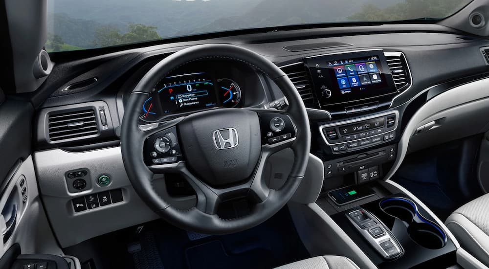 A close up of the grey and black interior of a 2022 Honda Pilot Elite shows the steering wheel and center console.