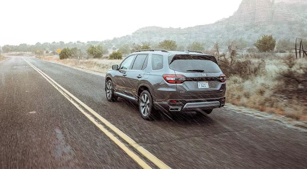 A grey 2023 Honda Pilot Elite is shown from the rear driving in the rain.