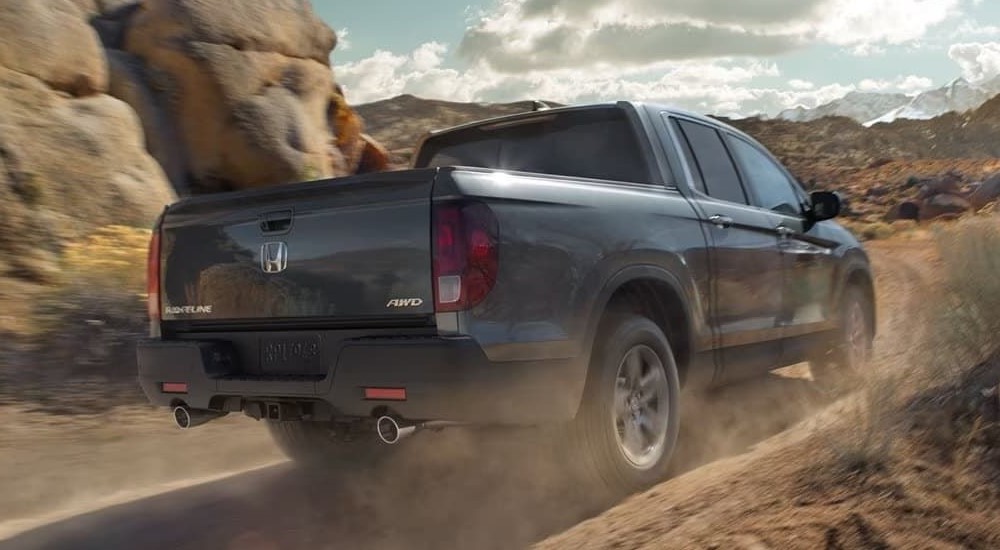 A grey 2023 Honda Ridgeline RTL-E is shown from the rear kicking up dust.