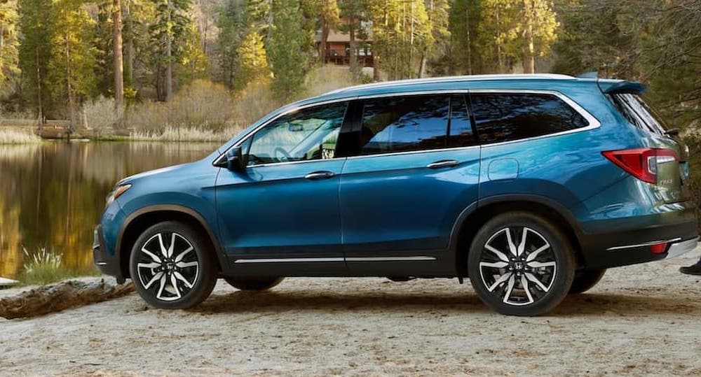 A blue 2021 Honda Pilot Elite is shown parked near a remote picnic area and body of water.