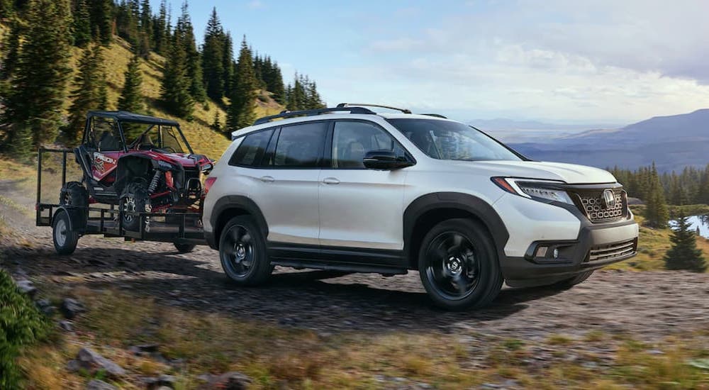 A white 2021 Honda Passport Elite is shown towing an ATV on a muddy trail.
