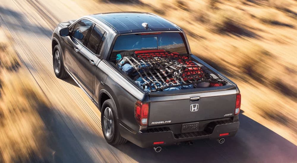 A grey 2022 Honda Ridgeline is shown with a full bed of a supplies while driving on a dirt road.