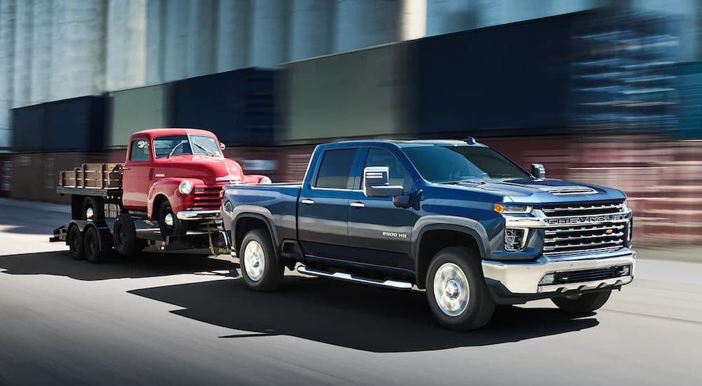 A blue 2022 Chevy Silverado 2500 is shown towing a red truck to a dealer that has used trucks for sale near Odessa.