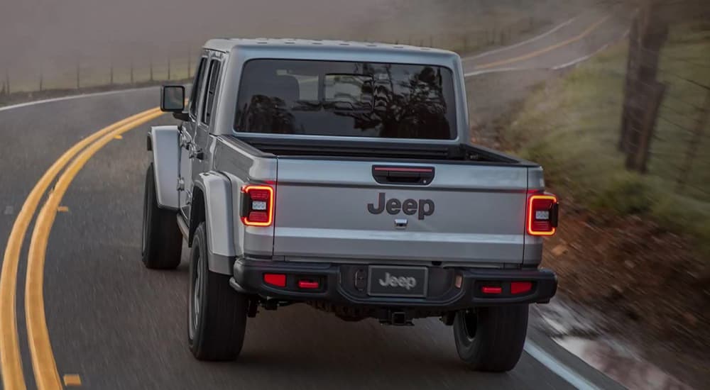 A silver 2022 Jeep Gladiator is shown from the rear driving on a winding foggy road.